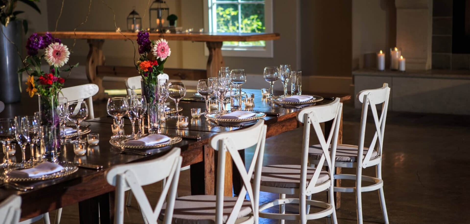 A long dark wood table set with flowers, cutlery and other tableware.