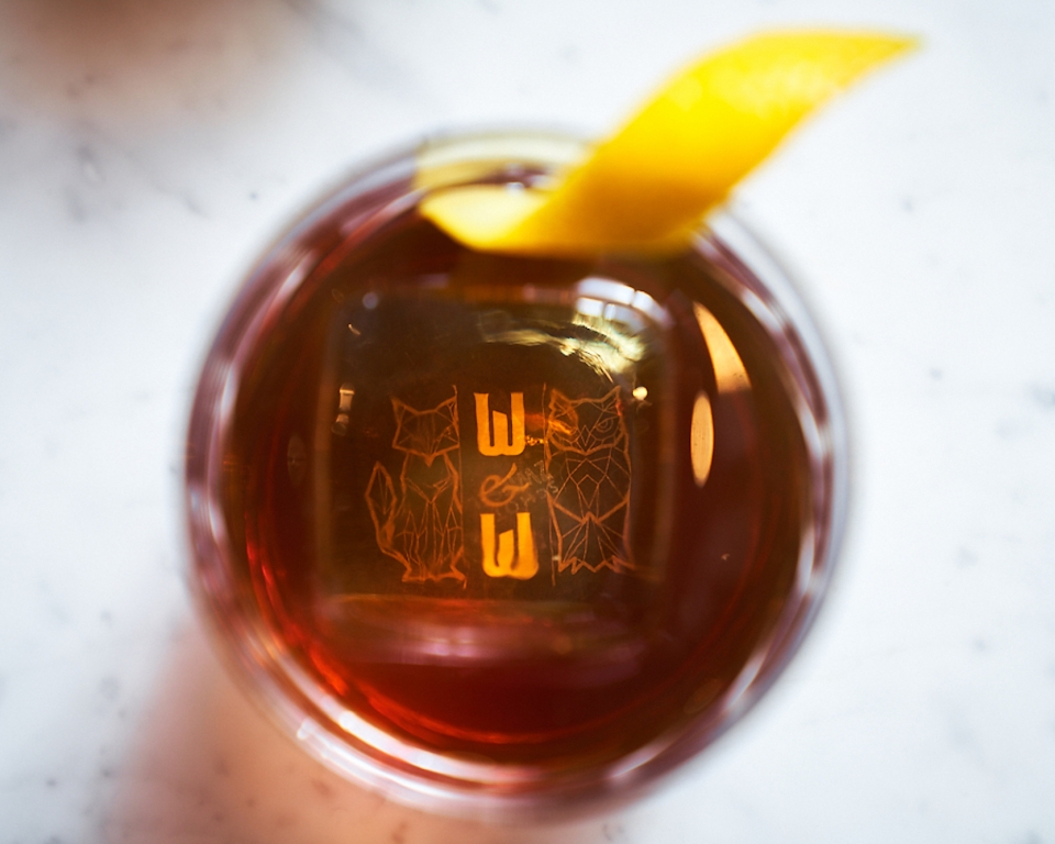 A cocktail with the Wit & Wisdom logo seen at the bottom of glass