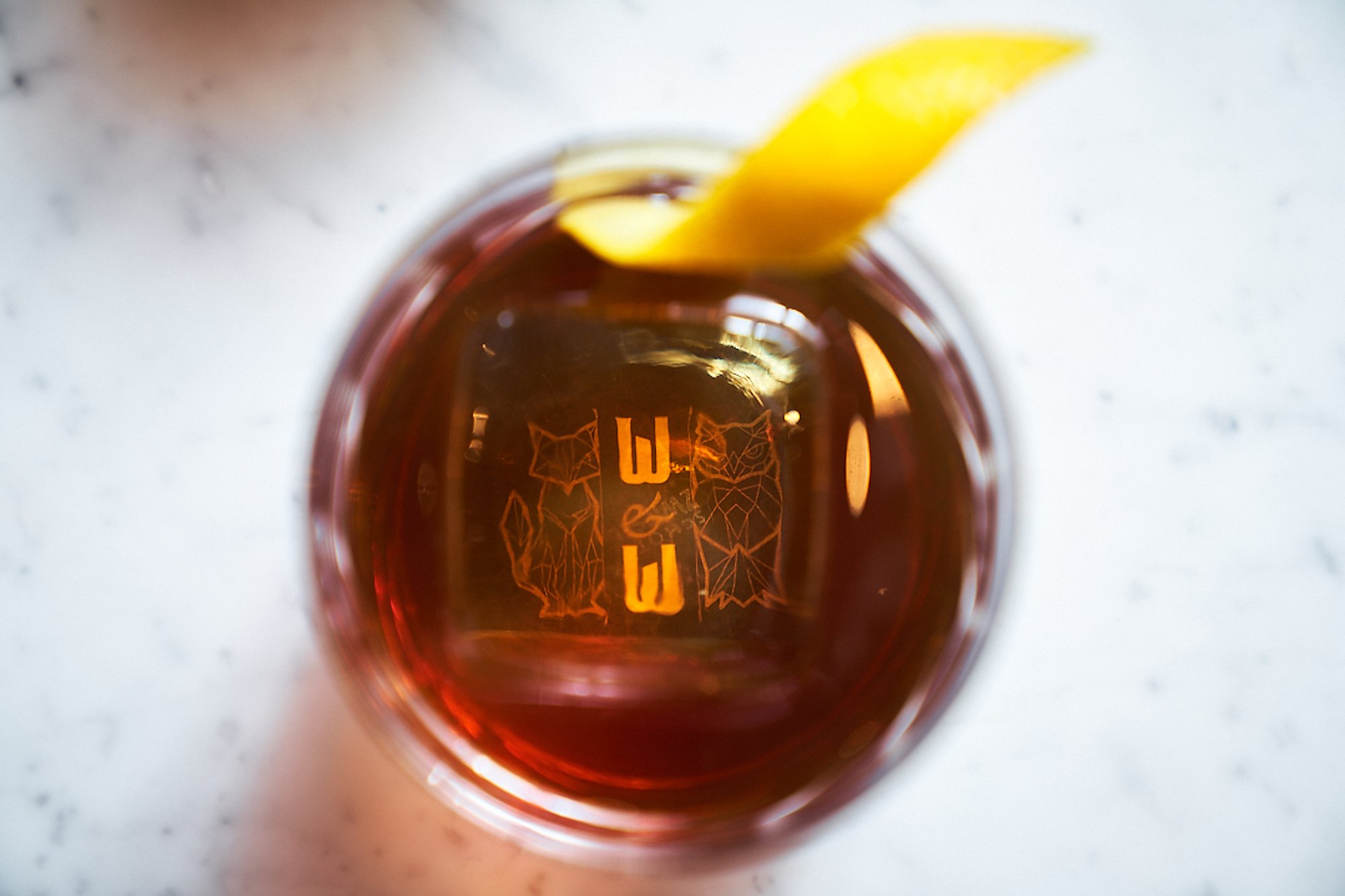 A cocktail with the Wit & Wisdom logo seen at the bottom of glass