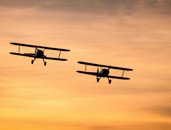Two biplanes flying together in the clouds at sunset.