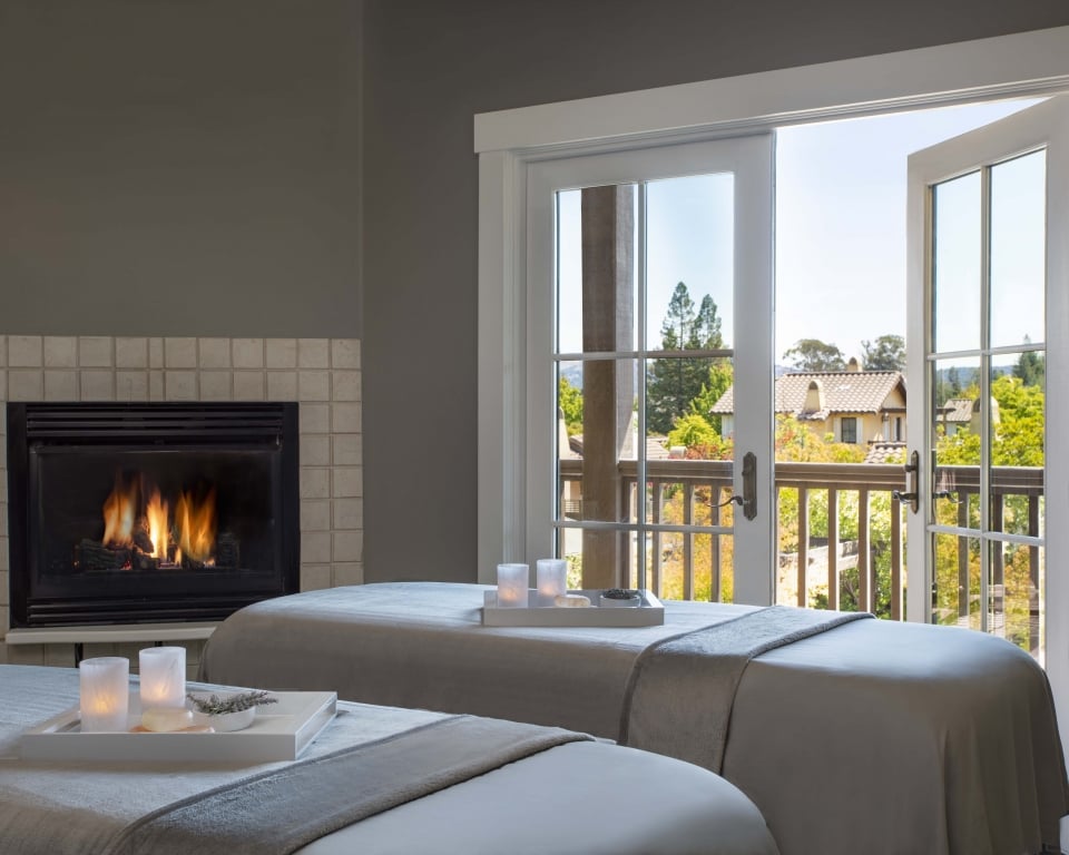 Spa Couples Treatment room with fireplace on and french doors opening to private balcony overlooking the spa garden