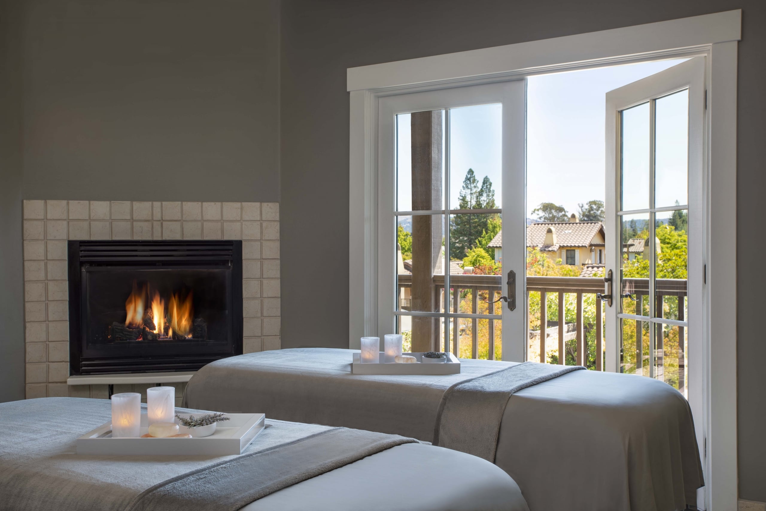 Spa Couples Treatment room with fireplace on and french doors opening to private balcony overlooking the spa garden
