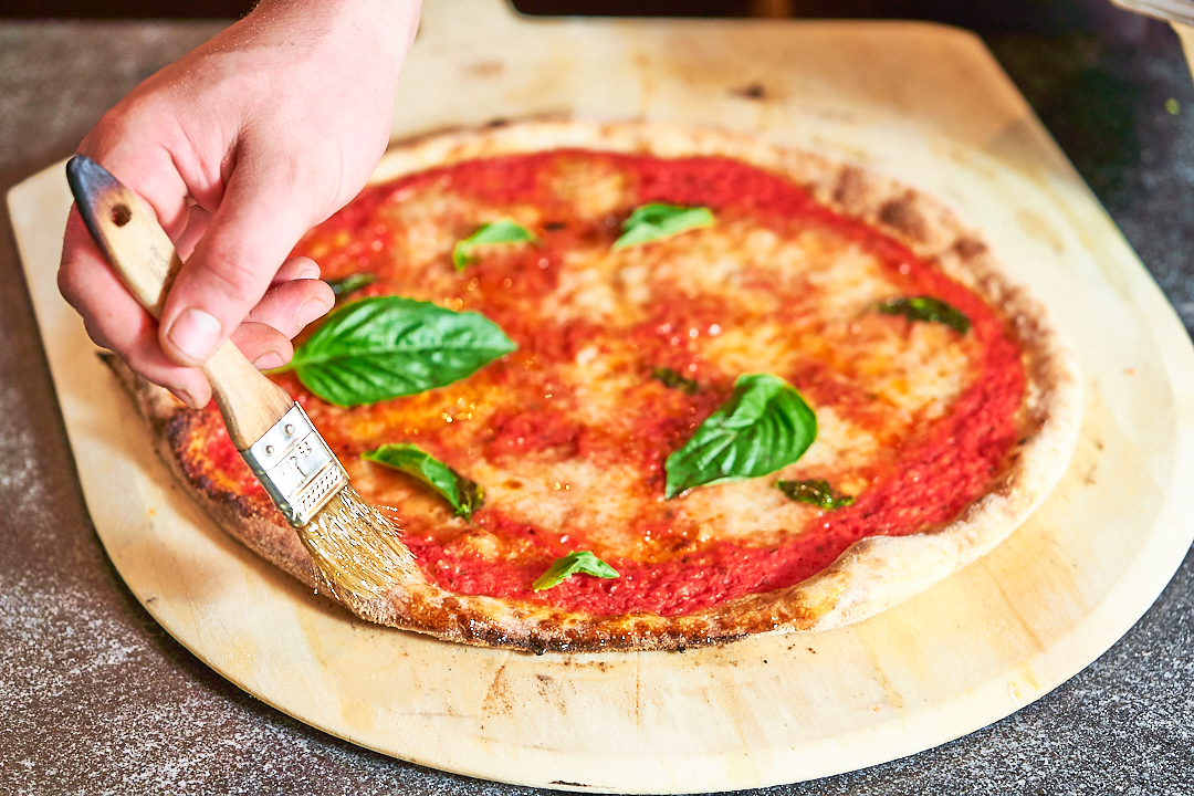 Pizza being brushed with olive oil