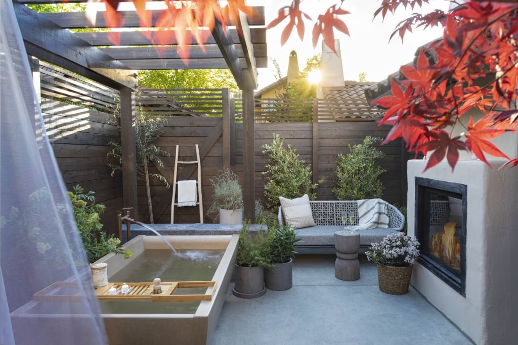 Luxurious spa courtyard with soaking tub, daybed, fireplace, and Japanese maples at sunset.