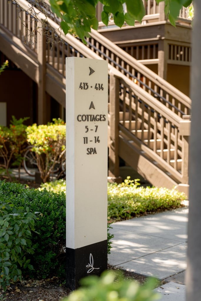 Elegant wayfinding sign for cottages and spa at luxury resort with white post and directional arrows among manicured greenery.