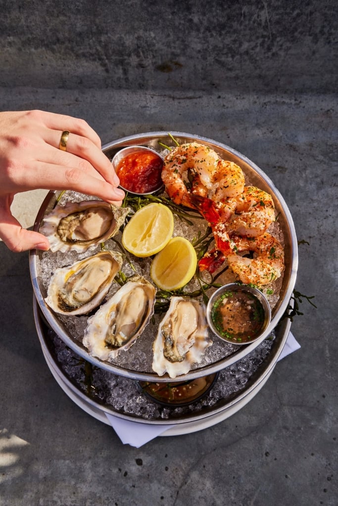 Elegant seafood tower with fresh oysters, garlic shrimp, and dipping sauces served on ice with lemon and rosemary.