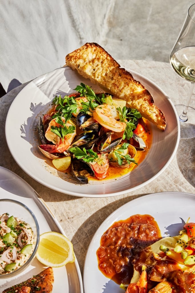 Plated seafood dish with mussels, shrimp, and clams in saffron broth, garlic bread, and white wine
