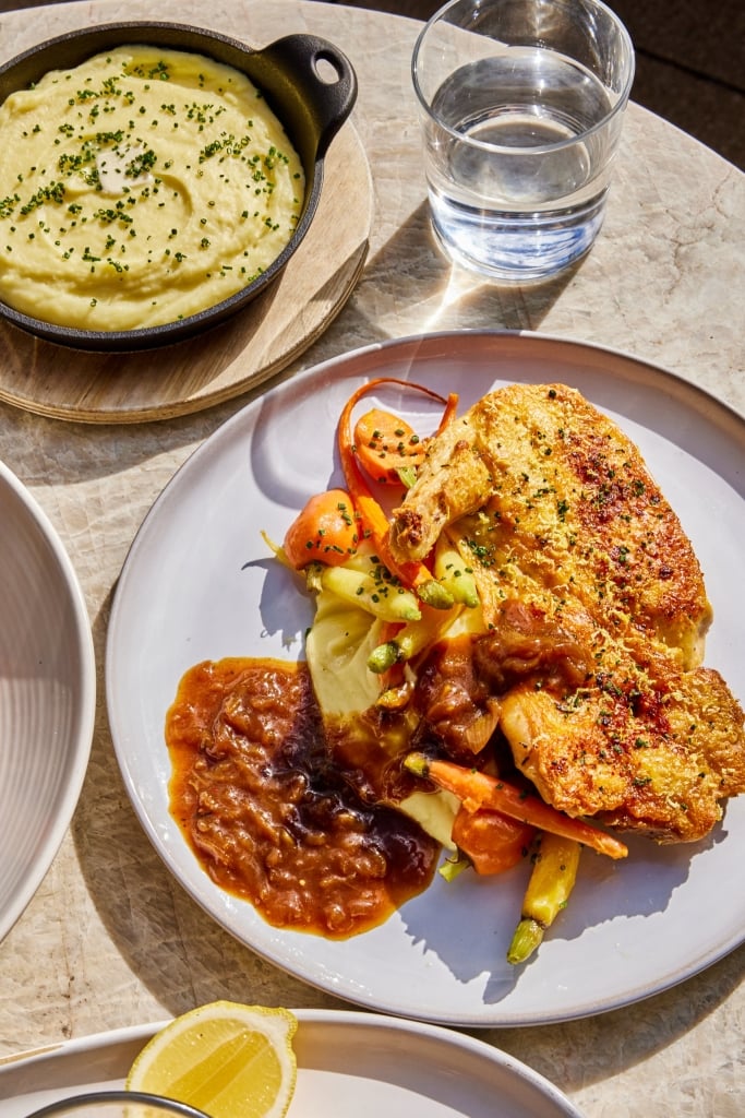 Luxury fine dining plate with golden-crusted protein, roasted vegetables, and rich sauce, paired with creamy polenta and water glass.