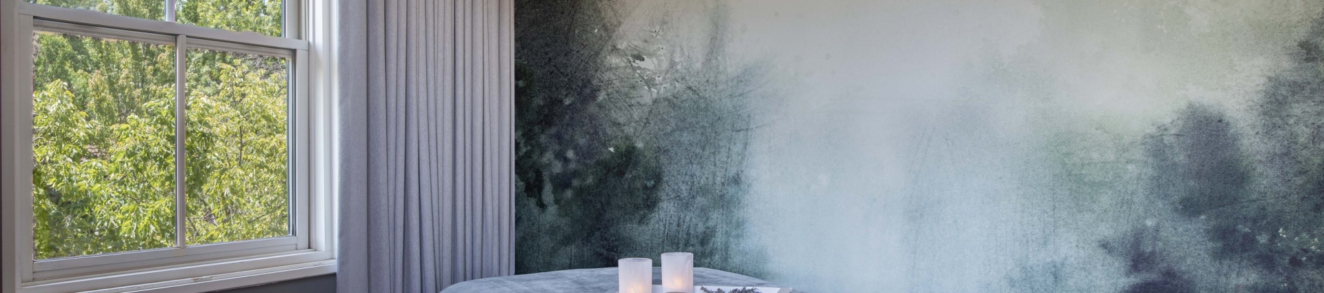 Serene spa treatment room with a massage bed, forest mural, candles, and a large window overlooking trees at The Spa at the Lodge at Sonoma