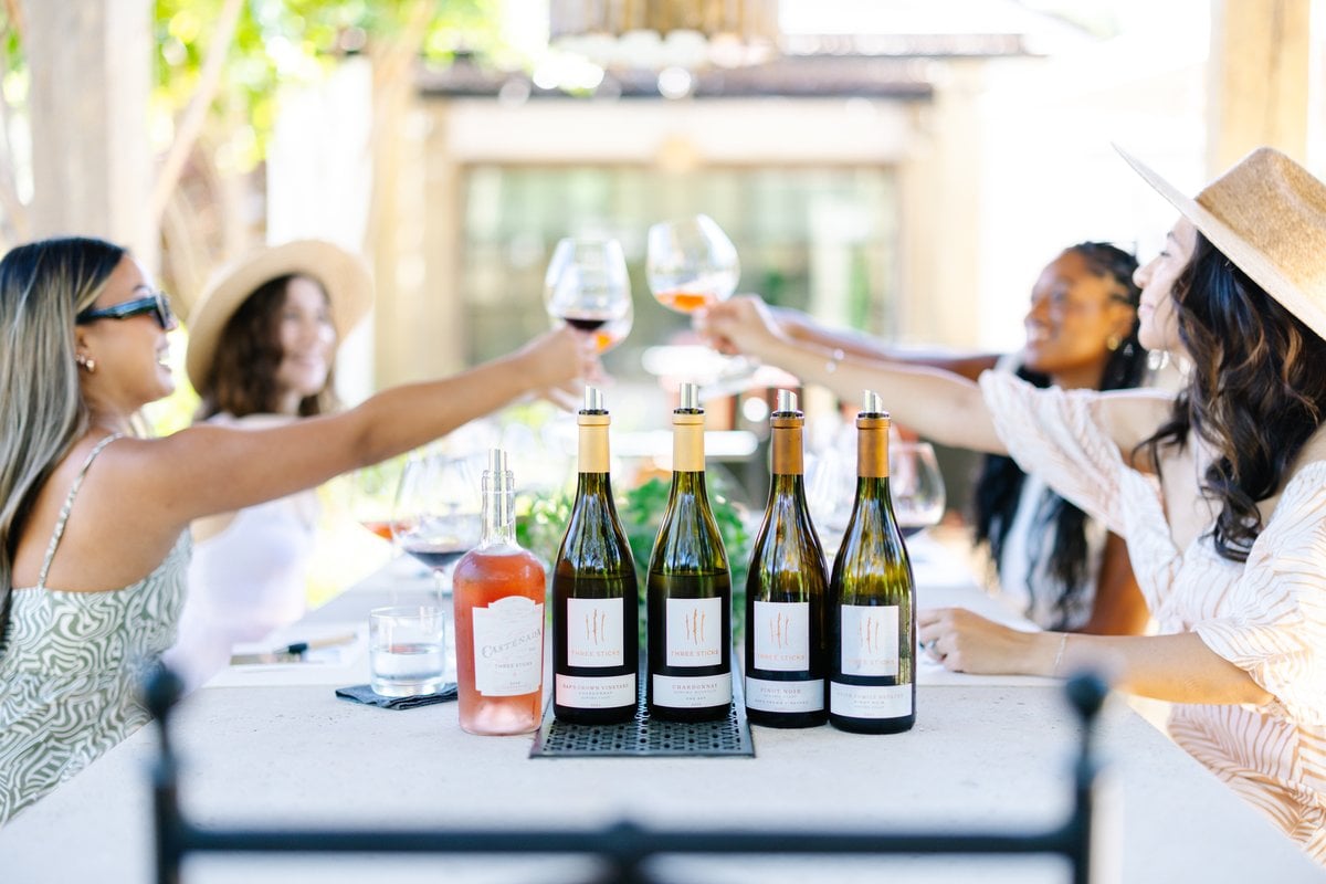 Guests toast with wine glasses over Three Sticks Winery bottles outdoors