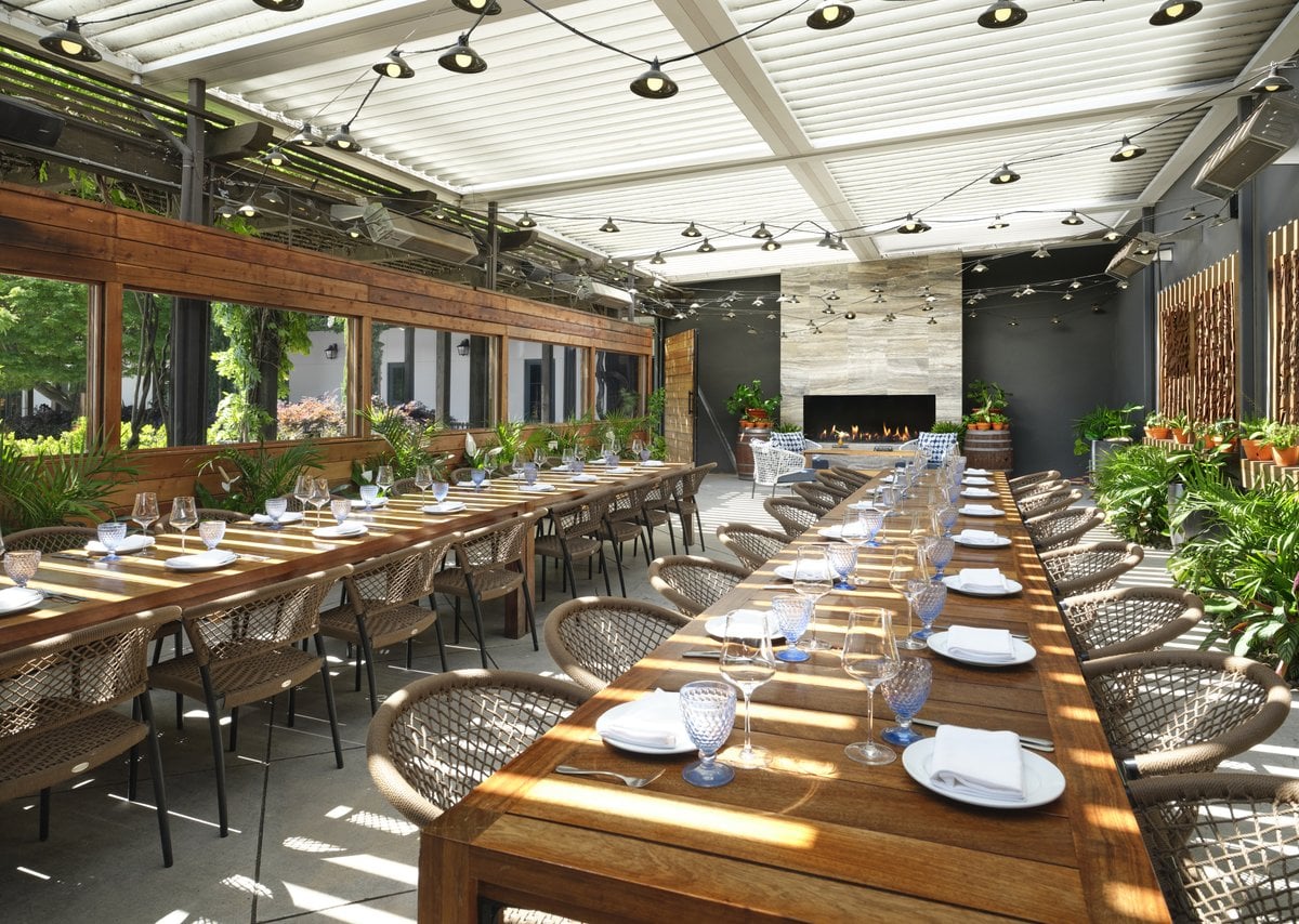 Sunlit private dining terrace with long wood tables and a stone fireplace